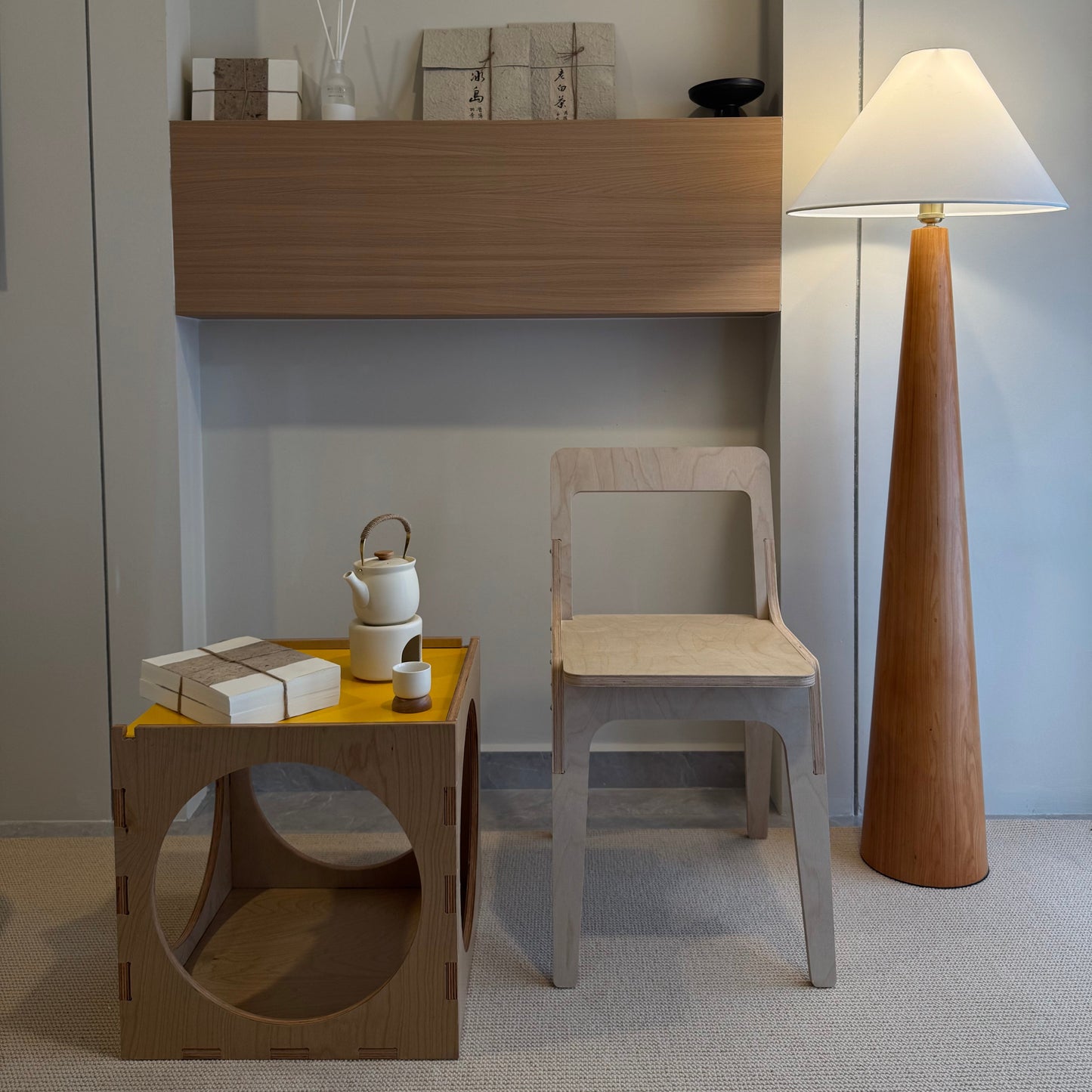 Modern interior with wooden shelf, chair, and lamp against a light gray wall.